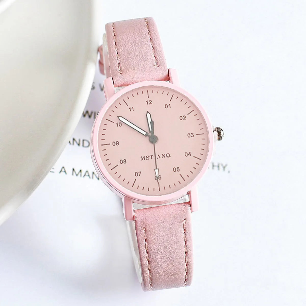 Pink wristwatch with minimalist dial and matching pink suede strap on a white background.