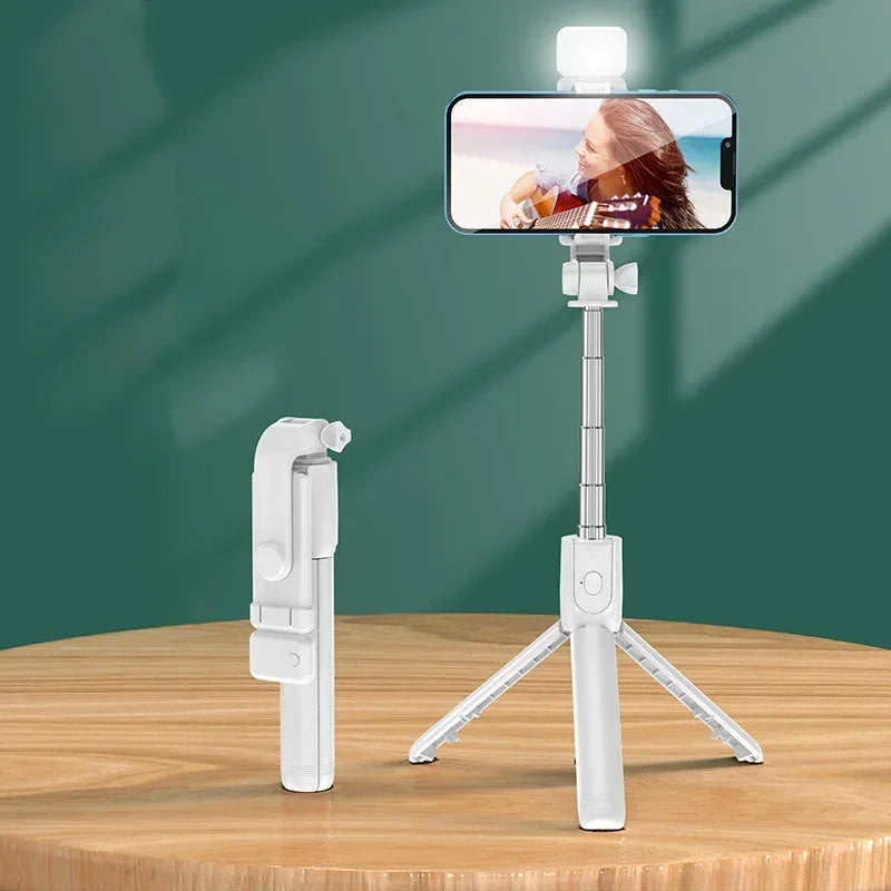 White selfie stick with smartphone holder on a wooden surface against a green background