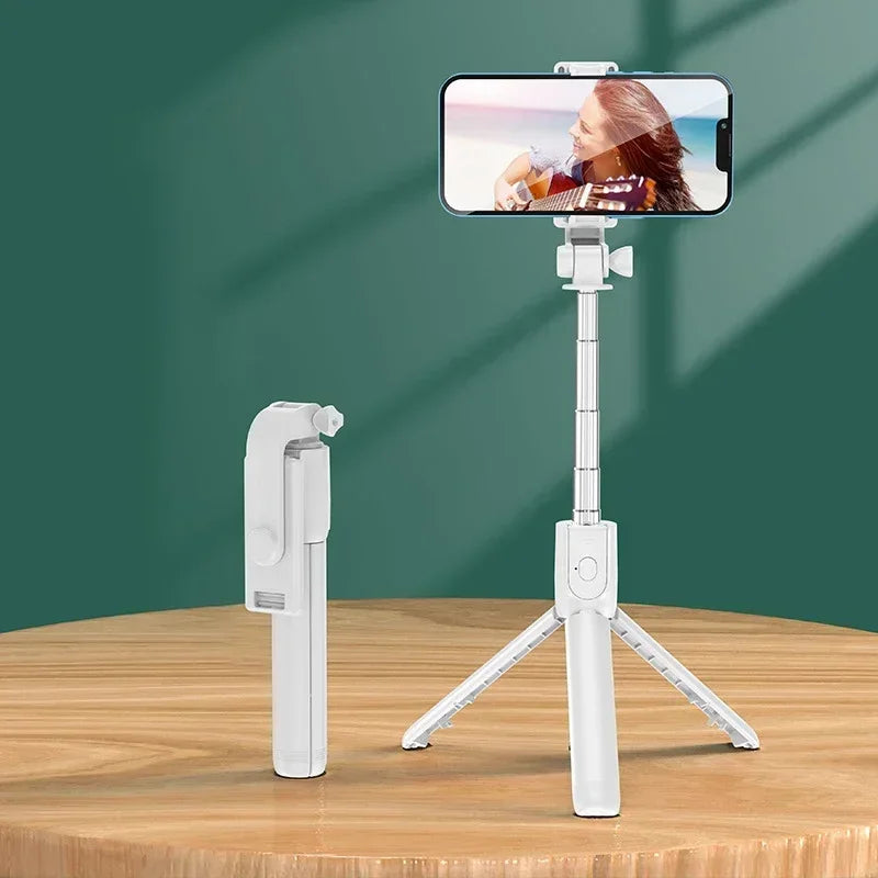 White smartphone selfie stick with remote control on a wooden surface and green background