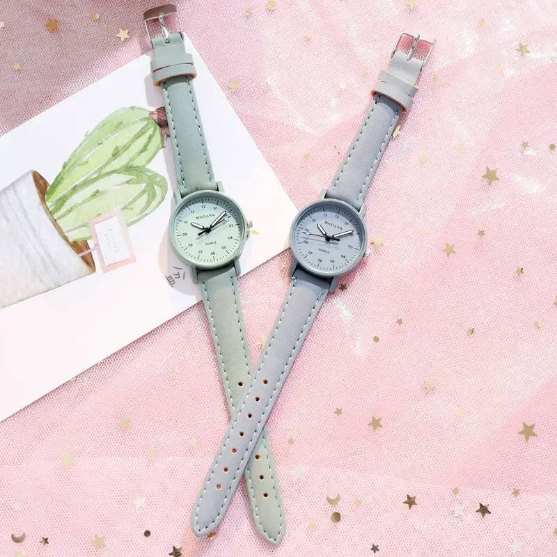 Two wristwatches, one green and one gray, placed on a pink star-patterned fabric with a cactus card.