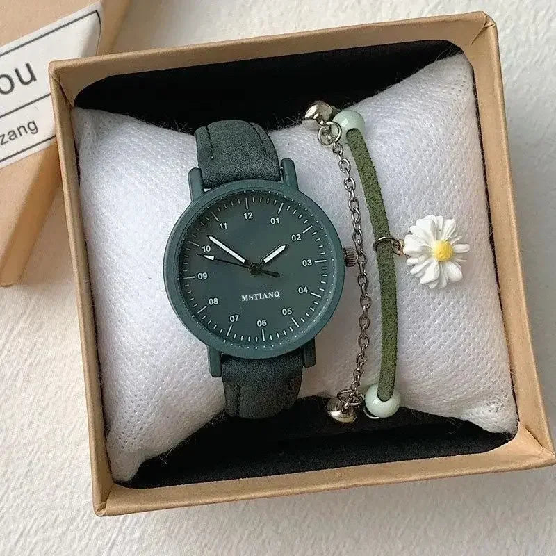 Green wristwatch with metallic hands and a matching bracelet featuring a white daisy charm, displayed in a gift box with a white cushion.