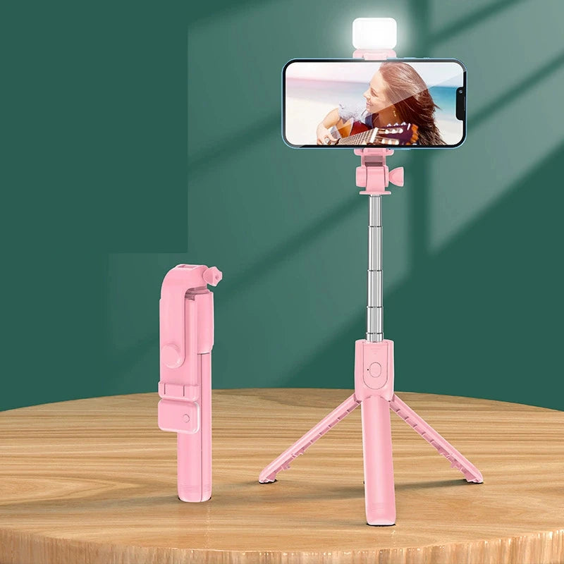 Pink selfie stick with smartphone holder on a wooden surface against a green background