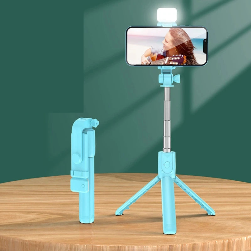 Blue selfie stick with phone holder on a wooden surface against a green background