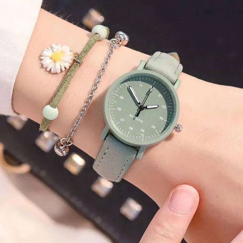 Green wristwatch with a minimalist dial, worn on a wrist alongside a green and white beaded bracelet with a daisy charm.