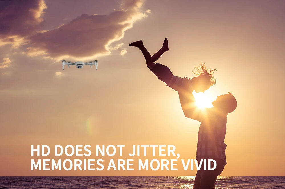 Person lifting child in the air with a drone flying overhead at sunset.