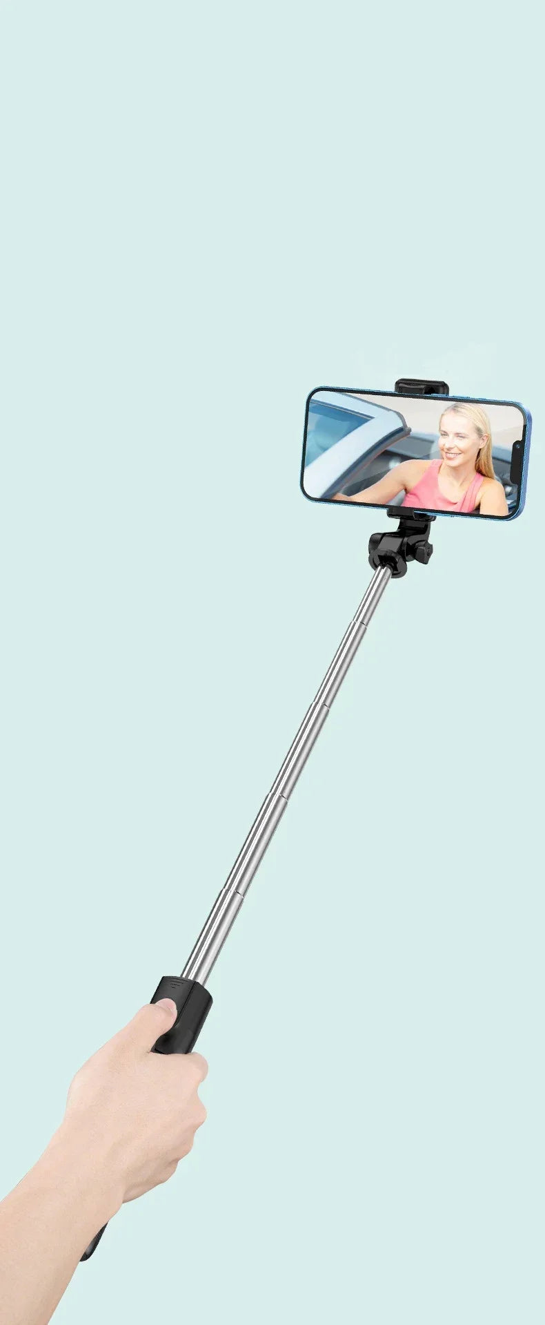 Hand holding a selfie stick with a smartphone displaying a person on a light blue background