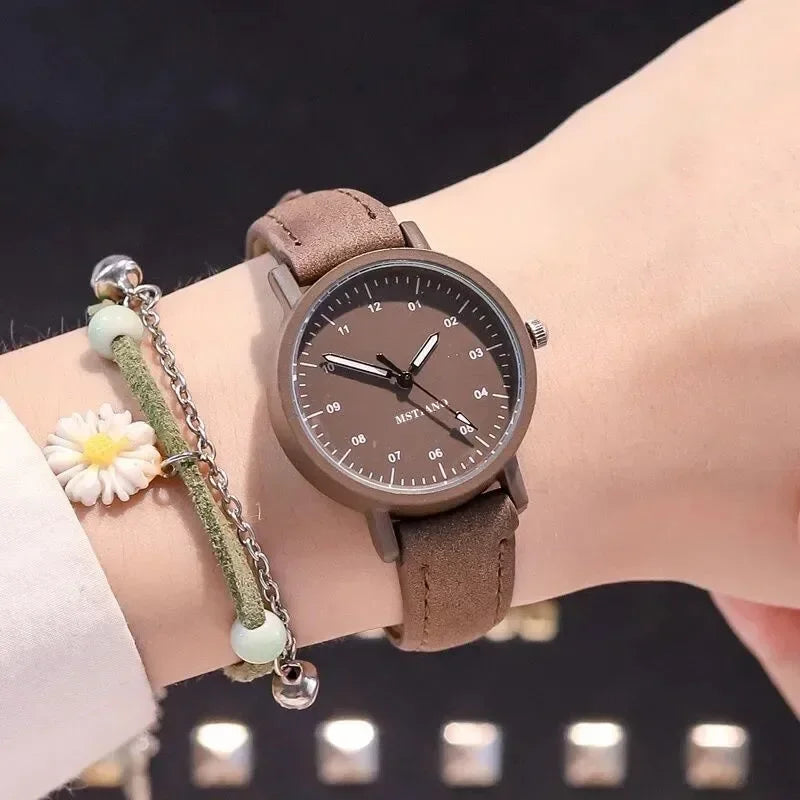 Brown wristwatch with minimalist dial, worn on wrist alongside a daisy charm bracele