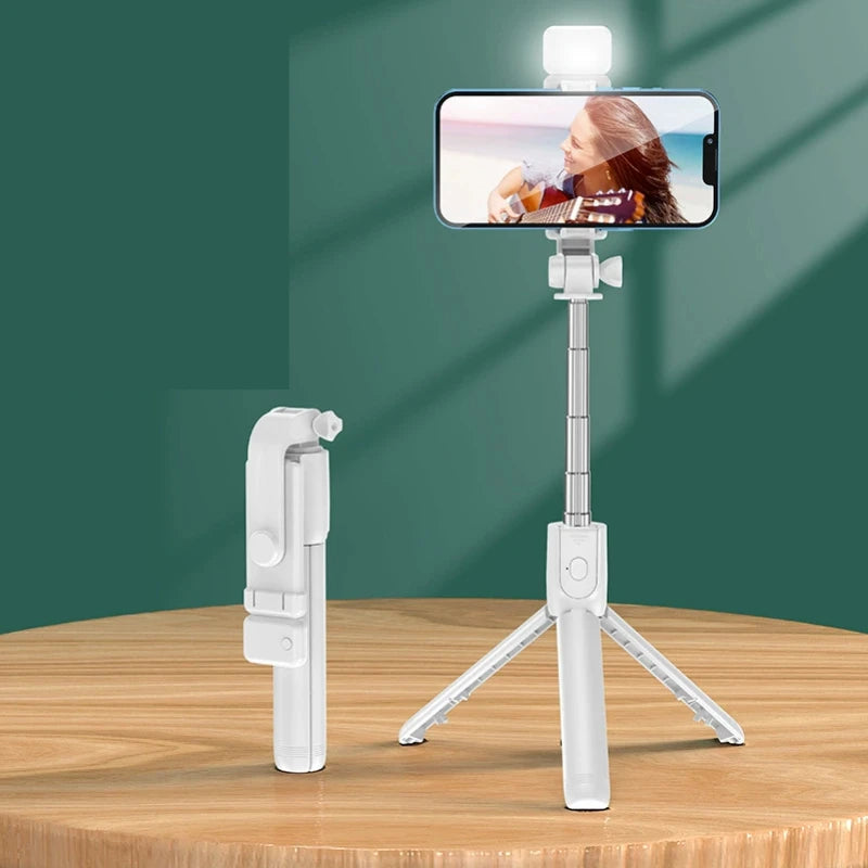 White selfie stick with smartphone holder on a wooden surface against a green background