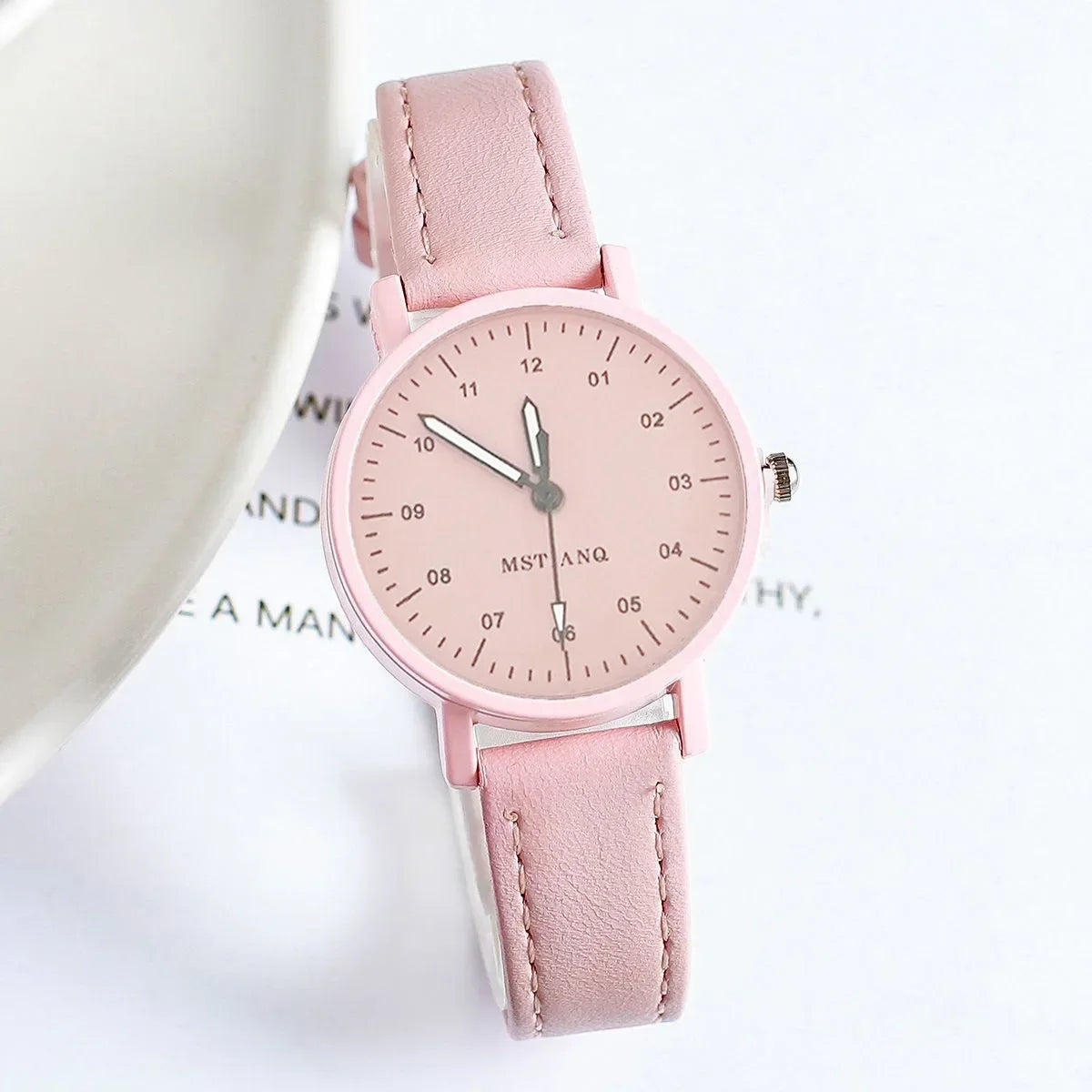 Pink wristwatch with minimalist dial and suede strap, displayed on a white surface.