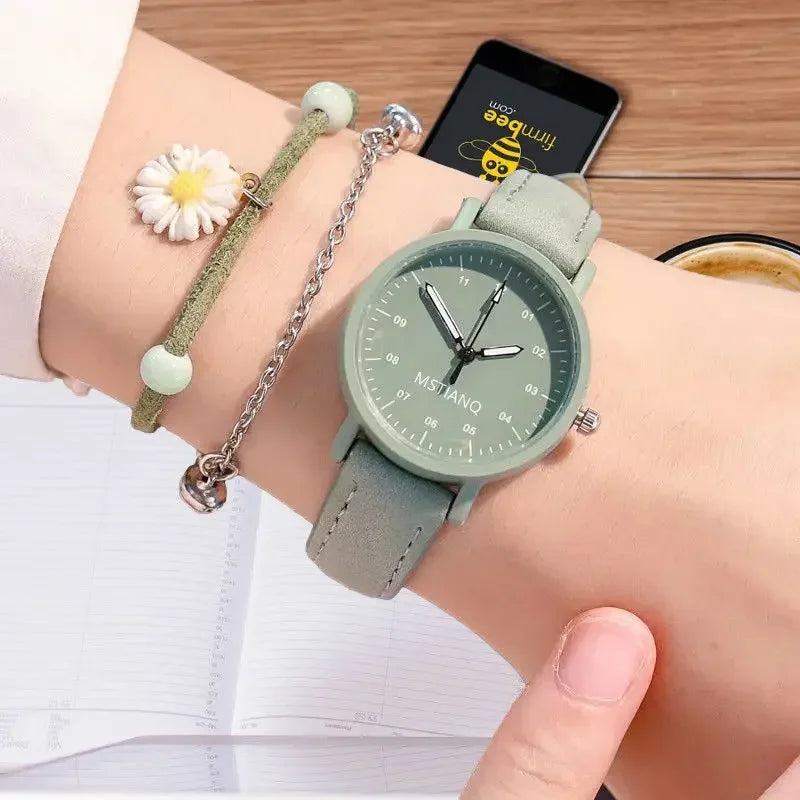 Green wristwatch with minimalist dial, paired with a green bracelet featuring a white daisy charm, displayed in a gift box.