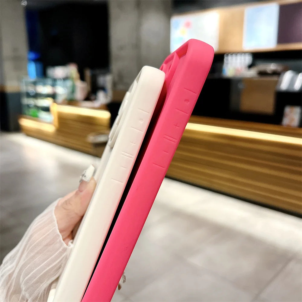 Two phone cases, one pink and one white, held against a blurred indoor background.
