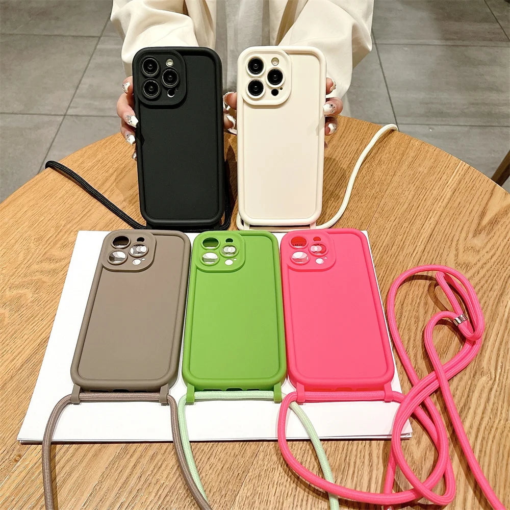Five phone cases in black, beige, green, and pink on a wooden table with a hand holding a black case.
