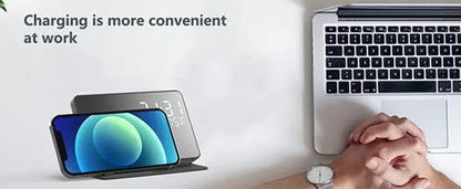 Person using a smartphone with a charging stand next to a laptop on a desk.
