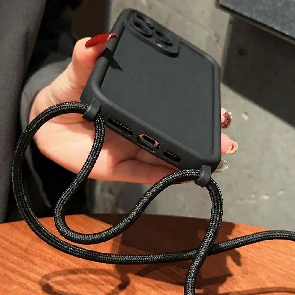 Person holding a black phone case with a lanyard on a wooden surface