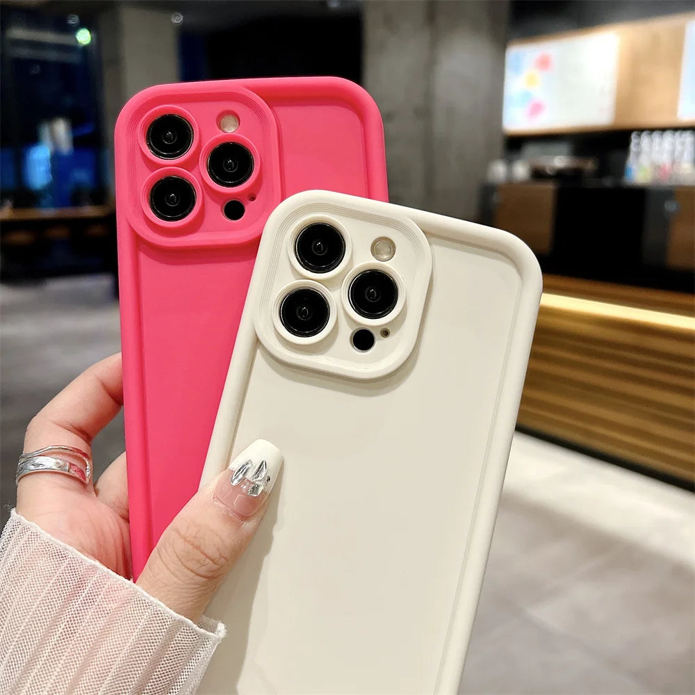 Two phone cases, one pink and one white, held by a hand with a blurred indoor background.